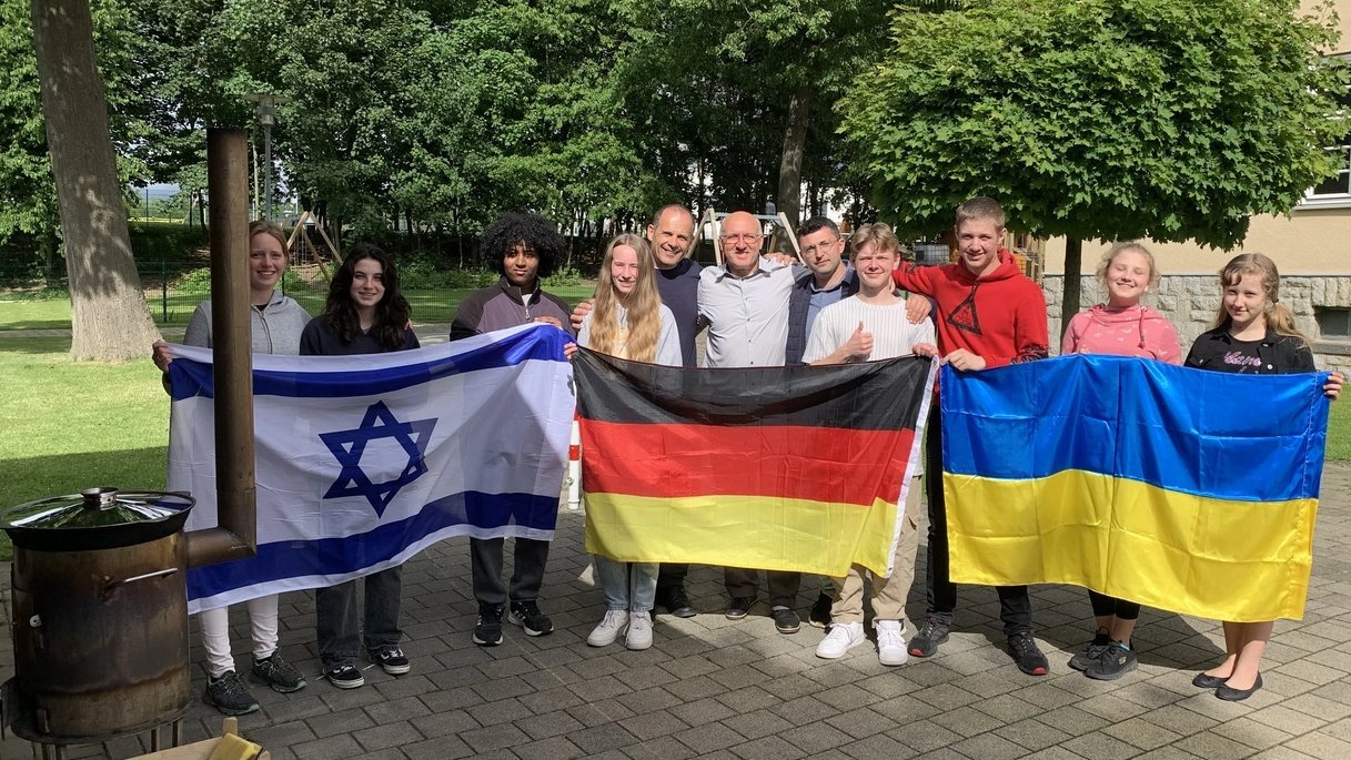 Eine Gruppe von Schülerinnen, Schülern und Lehrkräften hält vor sich die Flaggen von Israel, Deutschland und der Ukraine hoch